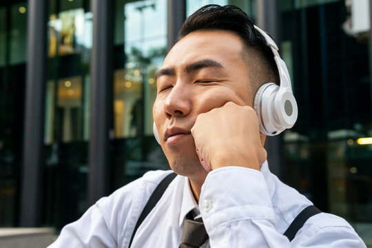 Sleepy ethnic businessman listening to music from headset on the street