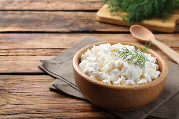 Fresh cottage cheese with dill in bowl on wooden table. Space for text
