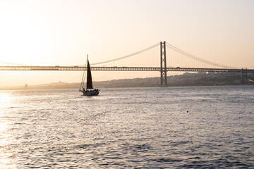 Sailing boat sailing in front of a bridge during sunset