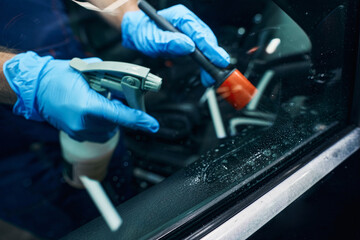 Auto mechanic cleaning window with spray from bottle