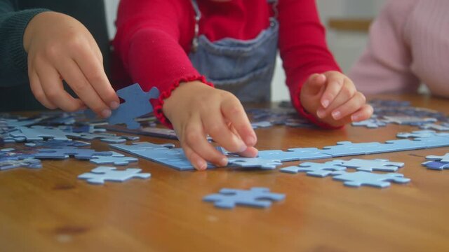 Close up of grandchildren with grandparents sitting around table at home doing jigsaw puzzle together - shot in slow motion