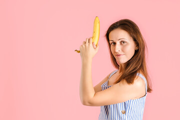 Cute brunette fooling around holding a yellow banana like a gun on a pink background. Copy space
