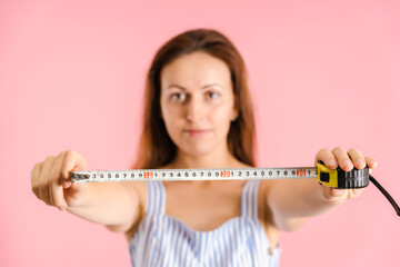 a woman shows the desired length of a man's penis using a measuring tape measure. Studio shot on a pink background, selective focus