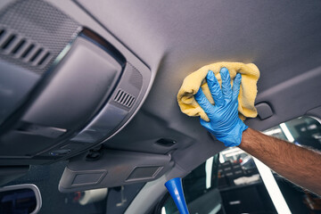 Worker wiping cleaning chemicals from automobile ceiling