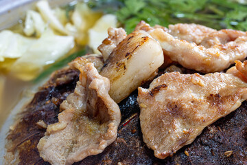A preparation of roasted meat with sauce of vegetable on Hot Pot - Mu Kratha, close up..Grilled slice pork at Thai Barbecue style, macro view.