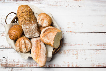 Assortment of baked bread into basket on wooden table. Top view