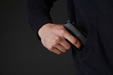 Man hiding gun in pocket against dark background, closeup