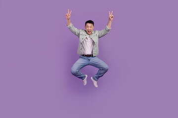 Photo of crazy positive friendly man jump show v-signs isolated purple color background