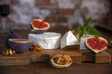 Cheese with white mold and figs lie on a cutting board .