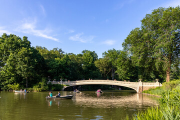 Tourists row a boat and take gondola ride on the Central Park Lake with Bow Lake background