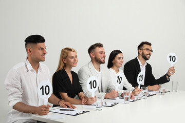 Panel of judges holding signs with highest score at table on white background