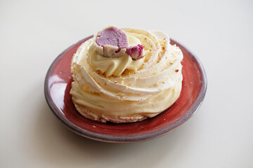 Pavlova dessert decorated with flower on a purple-red ceramic pottery plate on white background