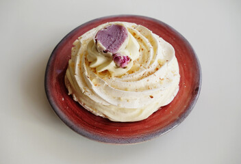 Pavlova dessert decorated with flower on a purple-red ceramic pottery plate on white background
