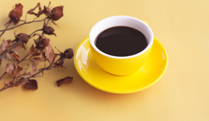 Yellow ceramic cup with black coffee put beside dried flower