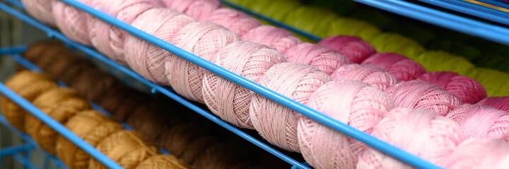 Fototapeta na wymiar rows of balls of colorful cotton yarn threads for knitting pale pink and mustard colors on the shelves in the store. banner