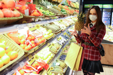 A young woman in a protective mask chooses fruit in the store