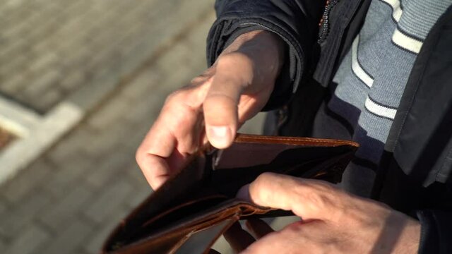 Empty Wallet in the Hands of an Elderly Man. An elderly man holds an empty purse. The concept of poverty in retirement .
