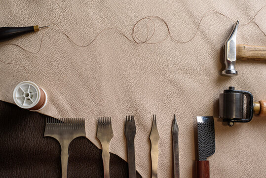 Shoemaking tools for sewing handmade shoes in workshop. Punches, awl, hammer, thread, roller on genuine leather. Workplace of shoemaker. Copy space.