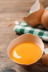 Cracked raw chicken egg with yolk on wooden table, closeup