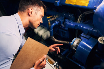 Concentrated experienced maintenance engineer examining diesel generator - obrazy, fototapety, plakaty