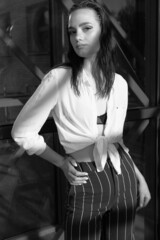 A melancholic black and white portrait of a young girl. A brunette in a white shirt and striped trousers is sitting on the steps	