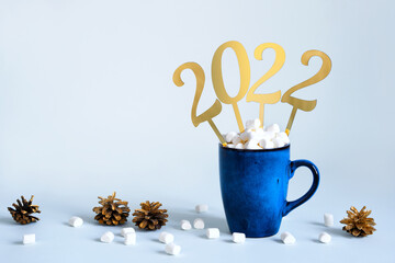 Christmas or New Year 2022 concept. Blue mug of cocoa with marshmallows and golden numbers 2022, copy space