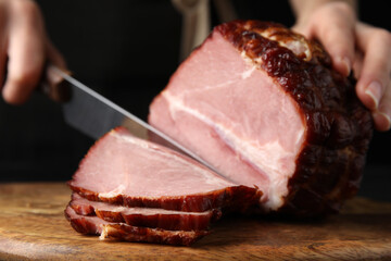 Woman cutting ham on wooden board, closeup