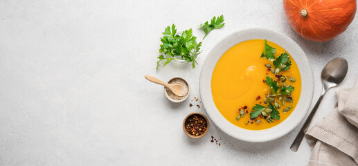 Pumpkin puree cream soup with seeds, spices and green parsley leaves in gray terracotta plate on white background. Autumn traditional food