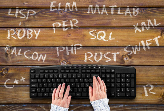 woman hands on PC keyboard and programming languages names on wooden table