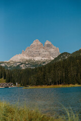 Auf dem Bild ist ein hoher Berg vor einem blauen Himmel zu sehen. Am Fuße des Berges liegt ein ruhiger See, umgeben von einem dichten Wald.