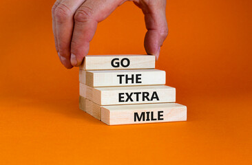 Go the extra mile symbol. Wooden blocks with words 'Go the extra mile'. Businessman hand. Beautiful orange background. Business and go the extra mile concept. Copy space.