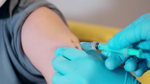 Close-up of doctor in medical latex gloves giving injection vaccine against coronavirus during mass vaccination campaign. Nurse using syringe to inject vaccine to patient prevent spread of covid19.