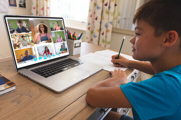 Biracial boy using laptop for video call, with waving diverse elementary school pupils on screen