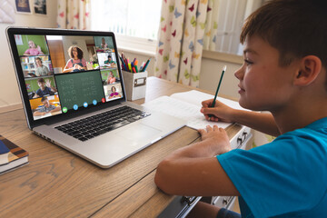 Fototapeta na wymiar Biracial boy using laptop for video call, with waving diverse elementary school pupils on screen