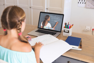 Obraz premium Caucasian girl using laptop for video call, with african american female teacher on screen