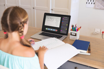 Caucasian girl using laptop for video call, with class on screen