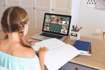 Caucasian girl using laptop for video call, with smiling diverse elementary school pupils on screen