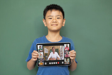 Smiling asian boy holding tablet for video call, with smiling elementary school pupils on screen