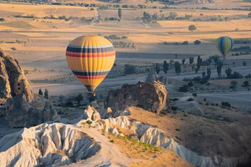 Poster heteluchtballon met regenboogkleurenpatroon dat oprijst boven de Cappadocische vallei © macondos