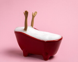 Hands sticking out of  red tub full of foam. Spa concept. Pink background.