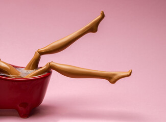Close up smooth legs of plastic toy doll in red hot bath on  pink background. Spa and depilation concept.