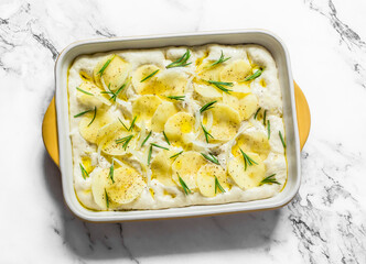 Raw Italian focaccia with potatoes and rosemary on a light background, top view. Cooking concept