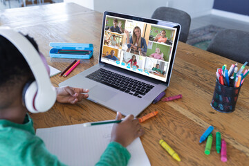 African american boy using laptop for video call, with diverse elementary school pupils on screen