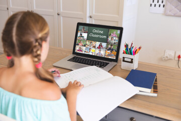 Caucasian girl using laptop for video call, with diverse elementary school pupils on screen