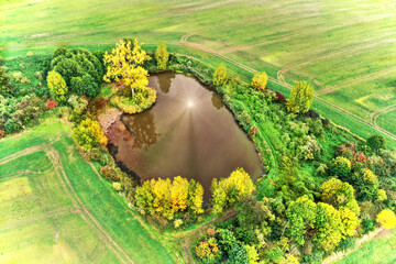 Aerial photo of a tiny brown pond, on the surface of which the rays of the sun are reflected