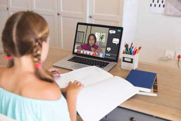 Caucasian girl using laptop for video call, with elementary school pupil on screen