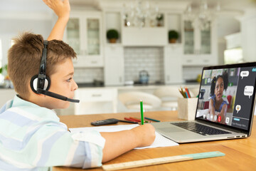 Caucasian boy raising hand for video call, with smiling elementary school pupil on screen