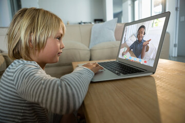 Smiling caucasian boy using laptop for video call, with elementary school pupil on screen
