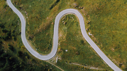 Aerial view of green fields, coniferous forest and narrow road in the Alps. Pathway in the mountains, directly above.