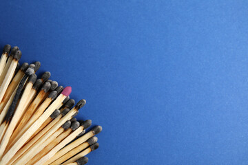 Heap of burnt matches and whole one on blue background, flat lay. Space for text